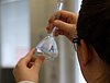 The picture shows a woman wearing a lab coat and protective glasses carrying and looking at a glass bulb in a laboratory