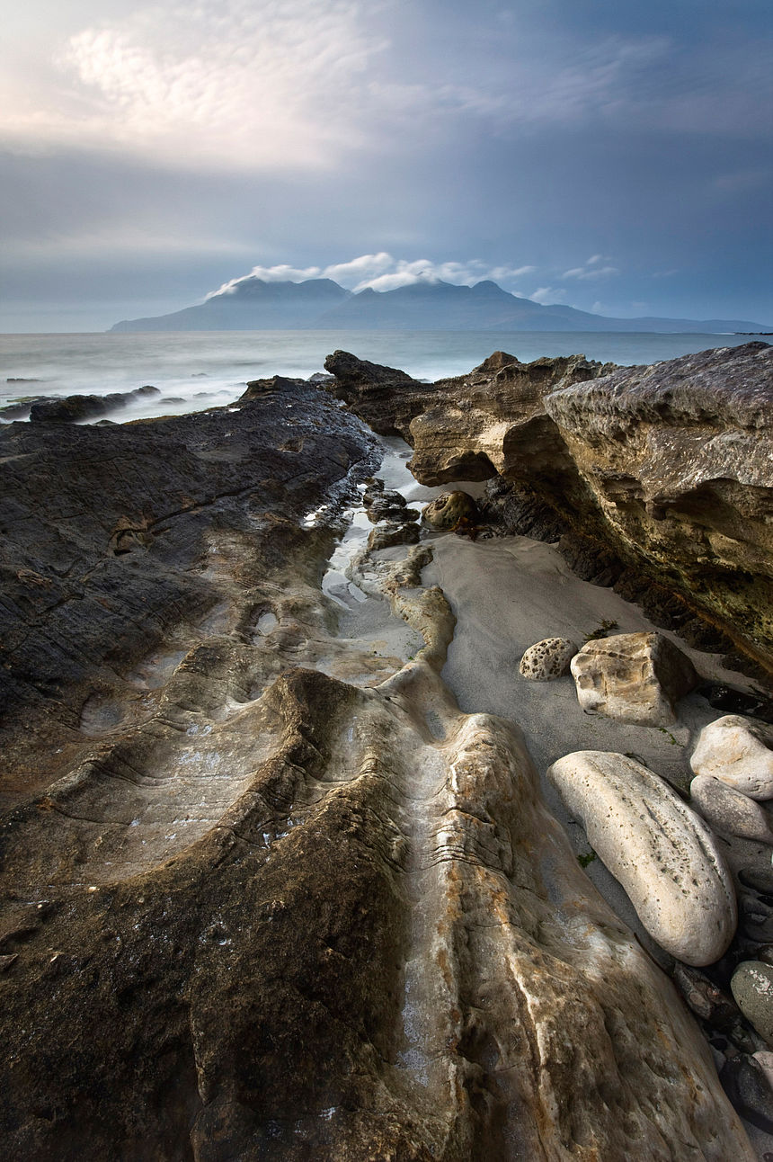 River deep, Mountain high A stone coast by the sea in front of a mountain landscape.